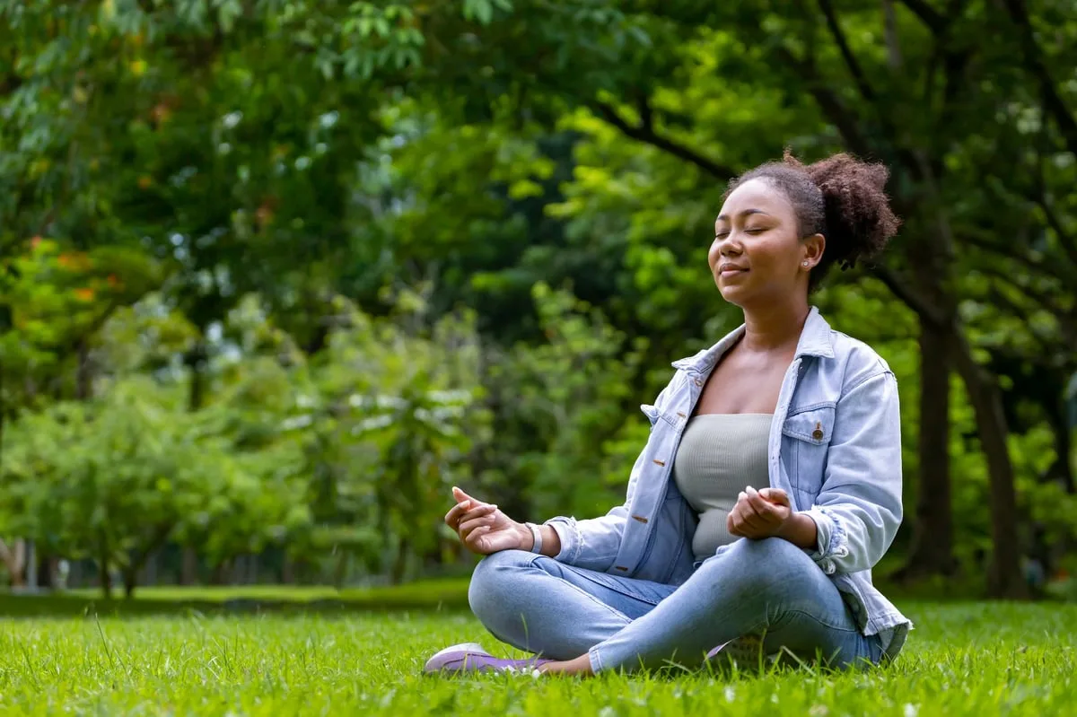 Mujer afroamericana meditando en el bosque representando paz interior y sabiduría para mente y alma