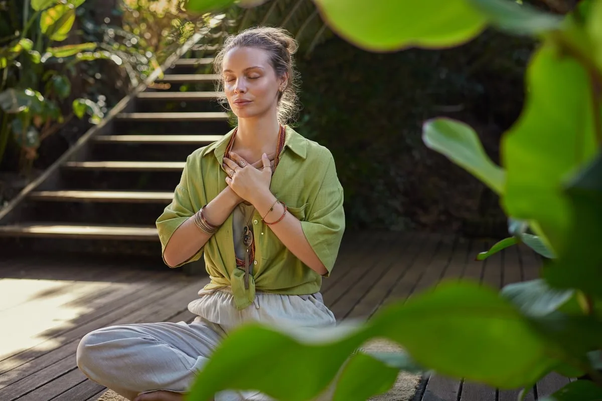 Mujer en meditación con manos sobre el corazón, representando coaching holístico y conexión espiritual para bienestar integral