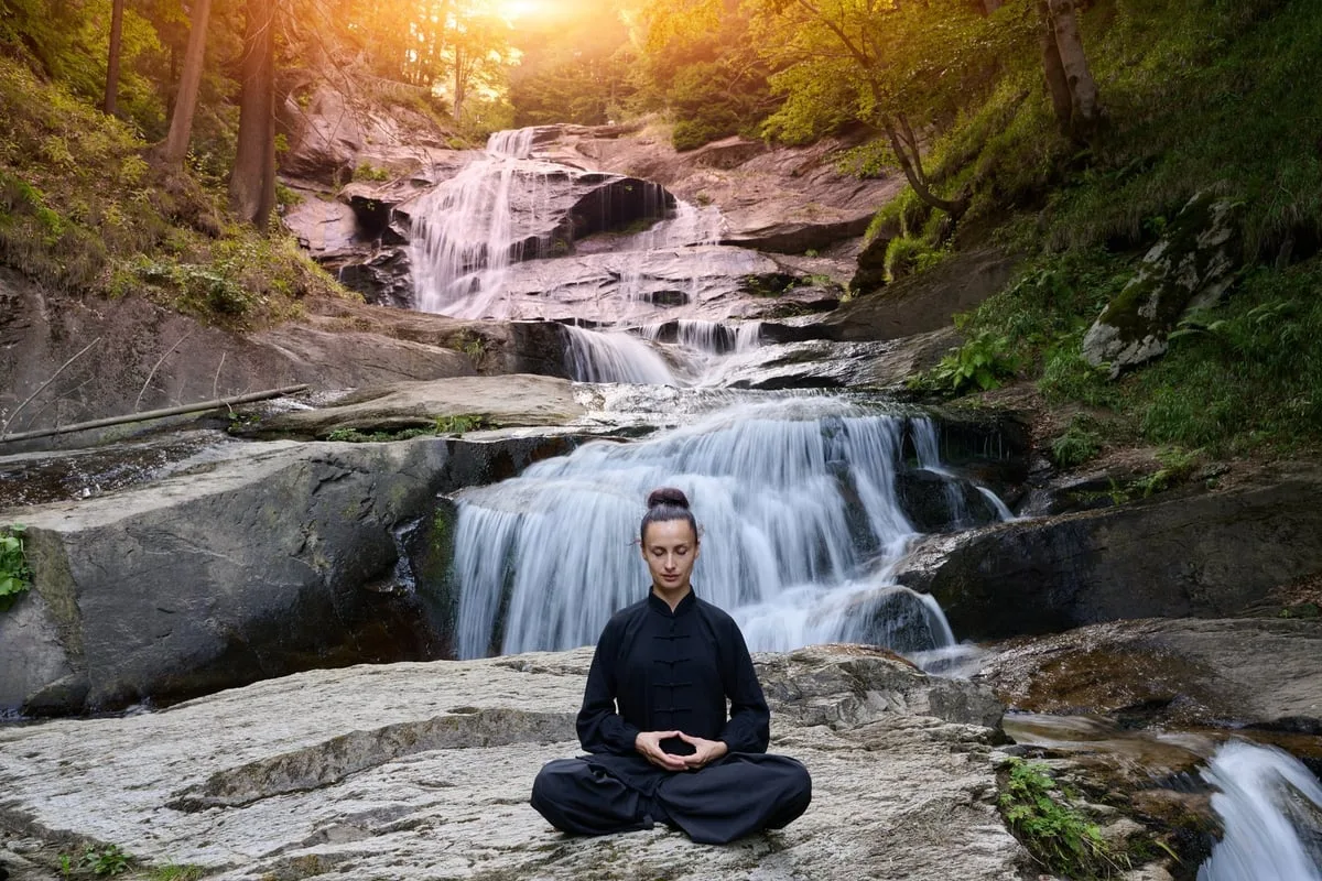 Mujer en postura de loto practicando yoga bajo cascada tropical representando conexión con la naturaleza y equilibrio interior