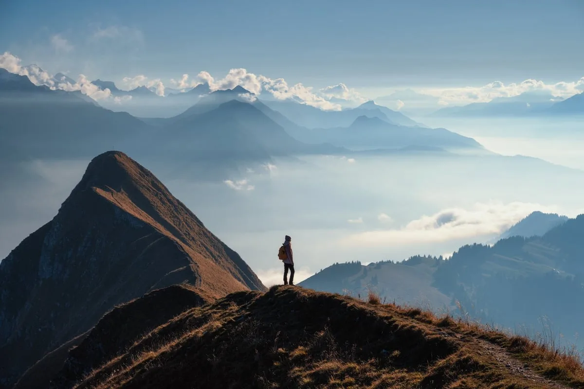 Mujer con mochila en montaña al atardecer representando camino de transformación y aventura espiritual